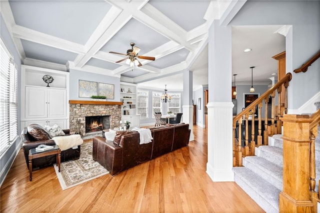 living room featuring stairs, ceiling fan with notable chandelier, light wood-type flooring, a fireplace, and ornate columns