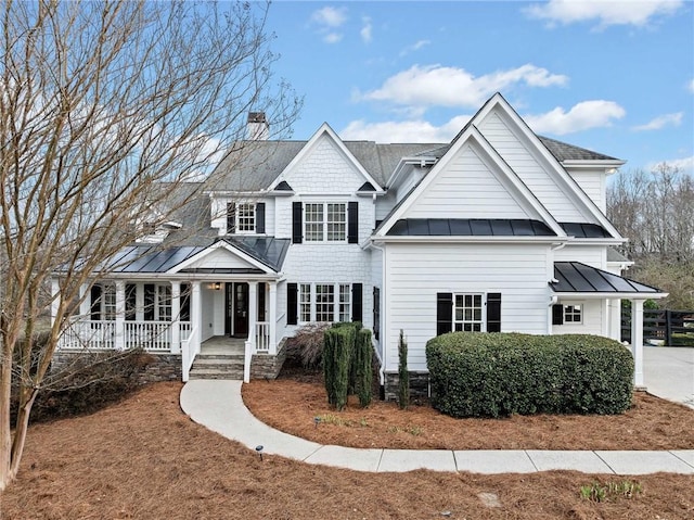 view of front facade with metal roof, a chimney, a standing seam roof, and covered porch