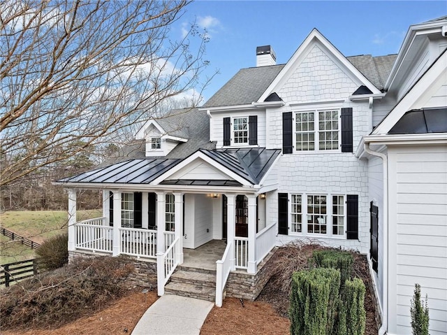 view of front of house featuring a chimney, a standing seam roof, covered porch, roof with shingles, and metal roof