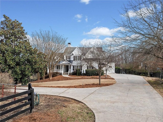 view of front facade with fence, a porch, a chimney, and curved driveway