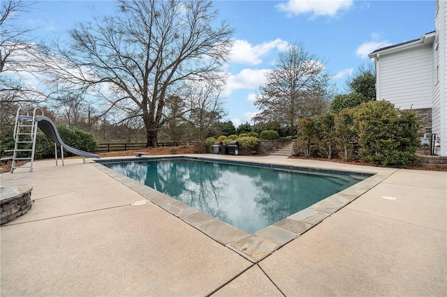 pool with a water slide, fence, and a patio area