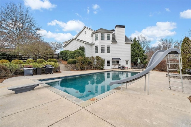 outdoor pool featuring a water slide, fence, a diving board, grilling area, and a patio