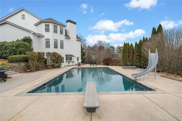 outdoor pool with a water slide, a patio, and a diving board