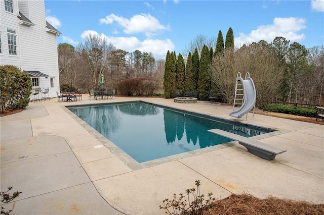 pool featuring a water slide, a diving board, a patio, and an outdoor fire pit