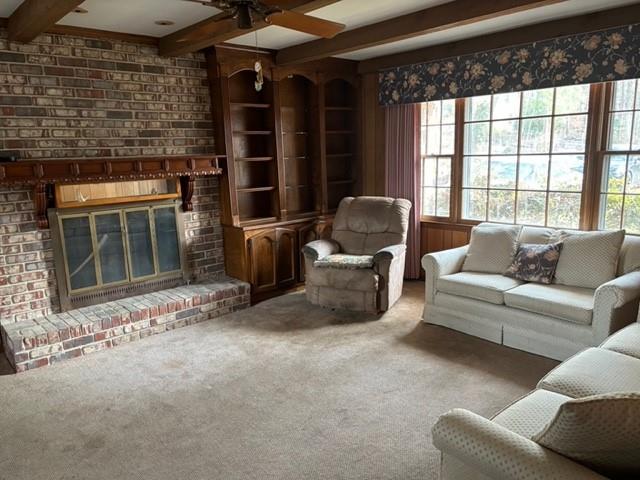 carpeted living room with ceiling fan, beam ceiling, a healthy amount of sunlight, and a brick fireplace