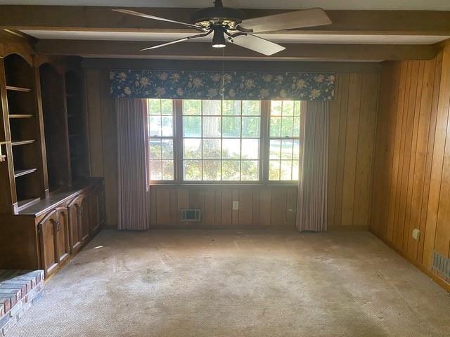 empty room featuring light carpet, ceiling fan, beamed ceiling, and wood walls