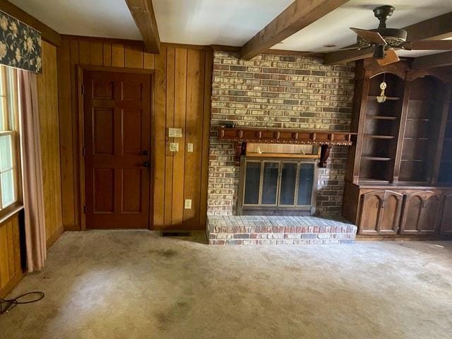 unfurnished living room featuring light carpet, a brick fireplace, beamed ceiling, and wood walls