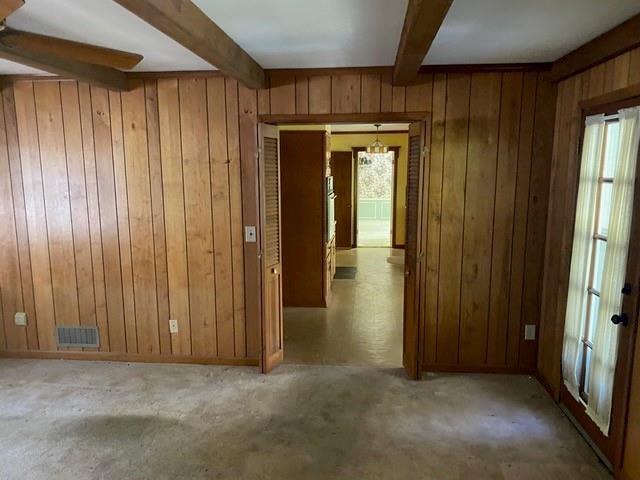 unfurnished room with light colored carpet, beamed ceiling, and wood walls