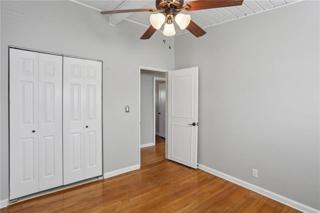 unfurnished bedroom featuring beamed ceiling, hardwood / wood-style flooring, wood ceiling, ceiling fan, and a closet