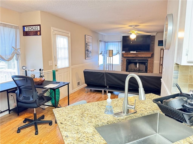 interior space with light stone countertops, ceiling fan, sink, light hardwood / wood-style flooring, and a fireplace