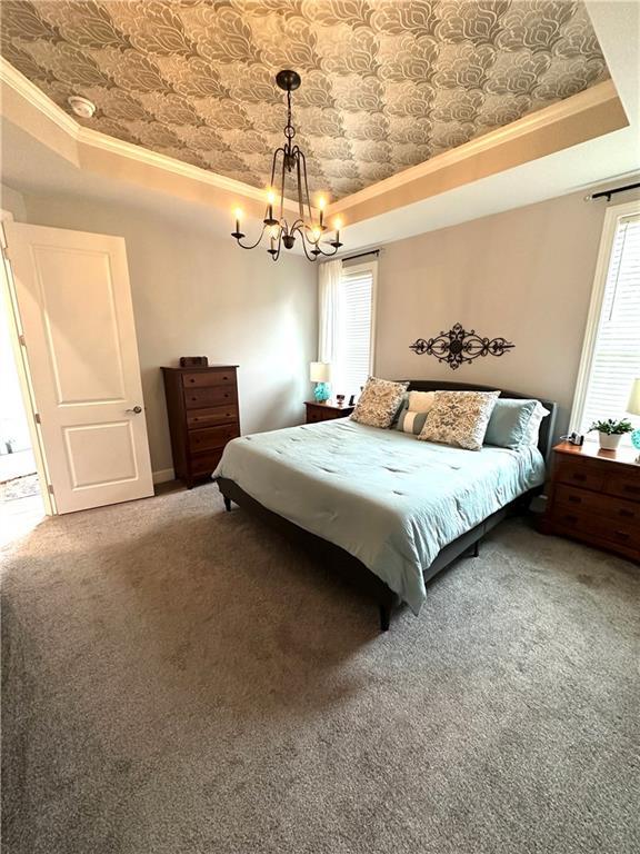 carpeted bedroom with a chandelier, a tray ceiling, multiple windows, and ornamental molding