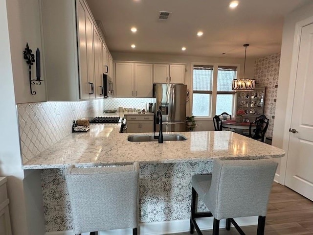 kitchen with sink, light stone countertops, appliances with stainless steel finishes, decorative light fixtures, and kitchen peninsula