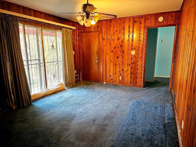 carpeted spare room featuring ceiling fan and wood walls