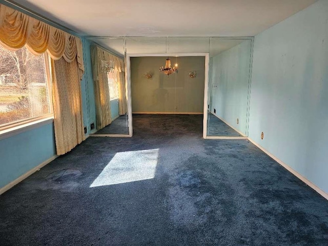 spare room with an inviting chandelier and dark colored carpet