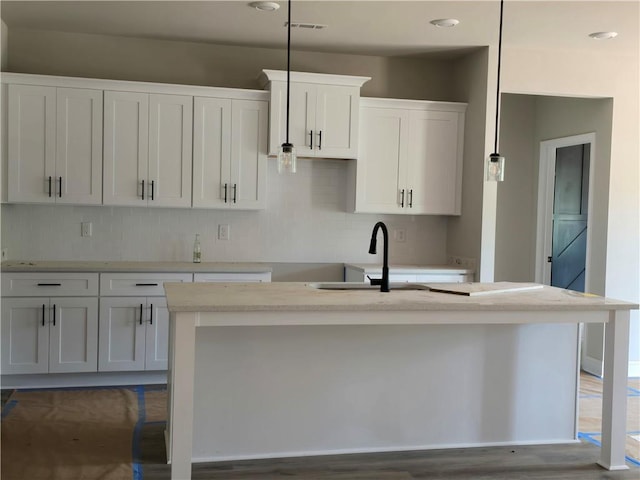 8970 Callaway Dr, Winston, GA 30187 - kitchen featuring a center island with sink, decorative backsplash, white cabinetry, a sink, and wood finished floors