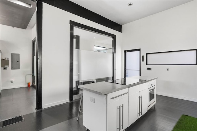 kitchen with white cabinetry, black electric stovetop, oven, a breakfast bar, and a kitchen island