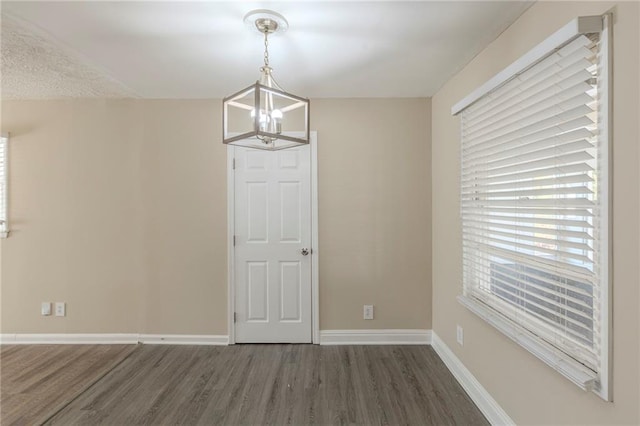 unfurnished dining area featuring a chandelier, baseboards, and wood finished floors