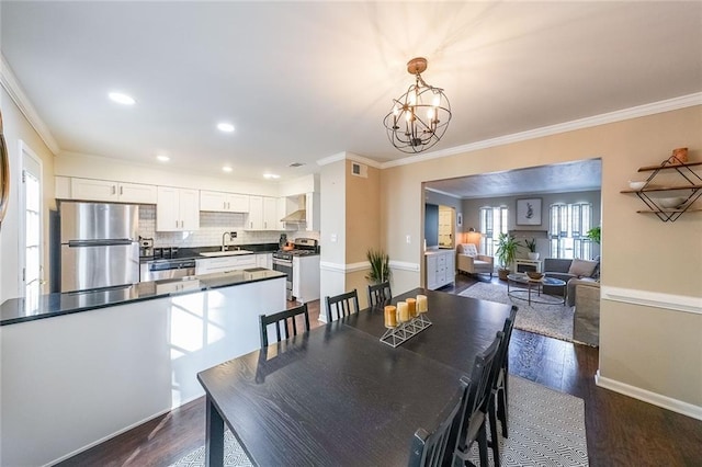 dining area featuring crown molding, sink, dark wood-type flooring, and an inviting chandelier