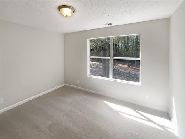 carpeted spare room with a textured ceiling, baseboards, and visible vents