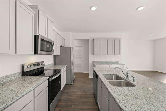 kitchen with light stone counters, appliances with stainless steel finishes, dark hardwood / wood-style flooring, sink, and white cabinets