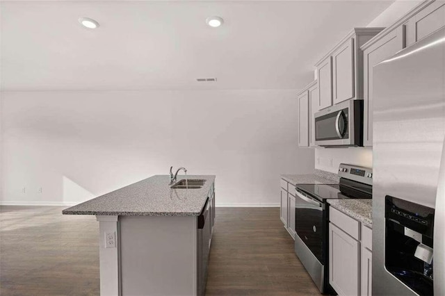 kitchen featuring a center island with sink, sink, appliances with stainless steel finishes, light stone countertops, and dark hardwood / wood-style flooring