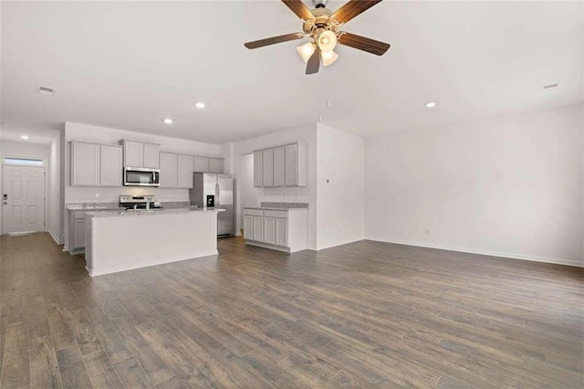 kitchen with light stone counters, stainless steel appliances, dark hardwood / wood-style flooring, ceiling fan, and a kitchen island with sink