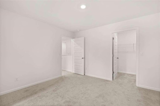 unfurnished bedroom featuring a closet, a spacious closet, and light carpet