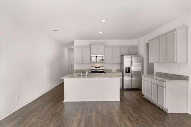 kitchen featuring stainless steel appliances, sink, light stone counters, dark hardwood / wood-style floors, and a kitchen island with sink