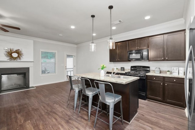 kitchen featuring decorative light fixtures, an island with sink, a kitchen bar, black appliances, and light stone countertops