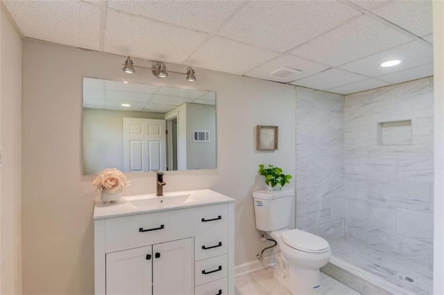 bathroom with a tile shower, tile patterned floors, toilet, a paneled ceiling, and vanity