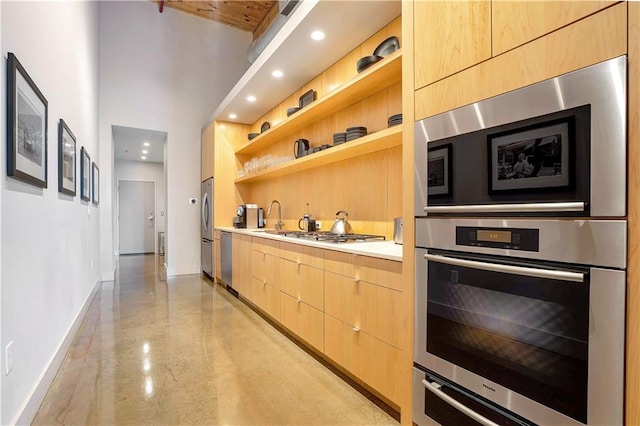 kitchen featuring light brown cabinets, stainless steel appliances, sink, and a towering ceiling