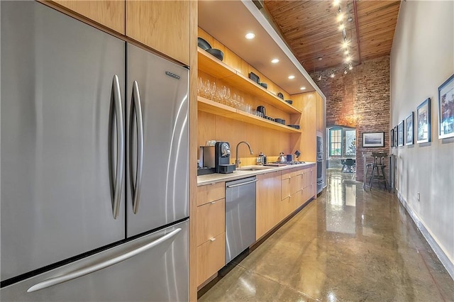 kitchen featuring brick wall, sink, stainless steel appliances, light brown cabinetry, and wood ceiling