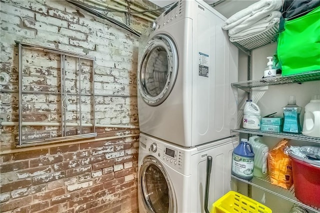 laundry area with stacked washer / dryer and brick wall