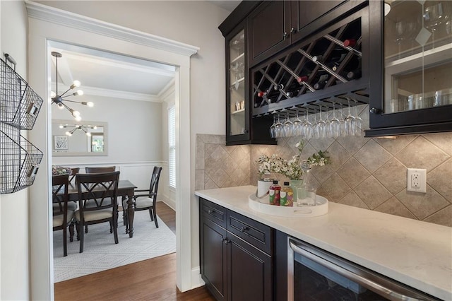 bar with an inviting chandelier, ornamental molding, dark wood-type flooring, wine cooler, and backsplash