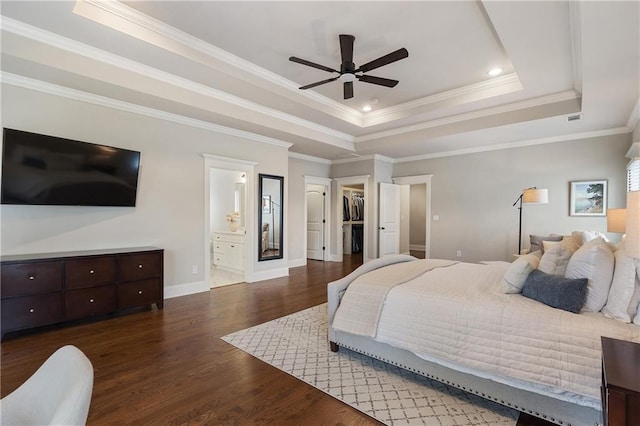 bedroom featuring wood finished floors, connected bathroom, baseboards, crown molding, and a tray ceiling