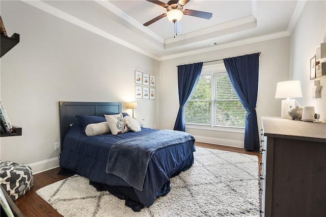 bedroom with baseboards, wood finished floors, ornamental molding, and a tray ceiling