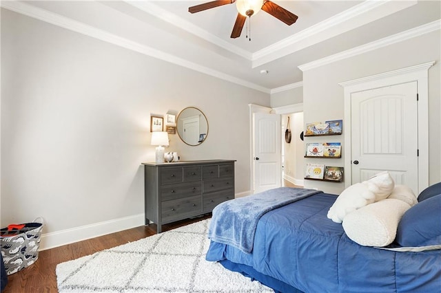 bedroom featuring wood finished floors, baseboards, a ceiling fan, crown molding, and a tray ceiling