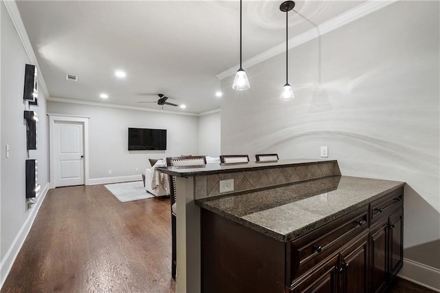 kitchen featuring dark wood-style flooring, a kitchen bar, ceiling fan, dark brown cabinetry, and ornamental molding