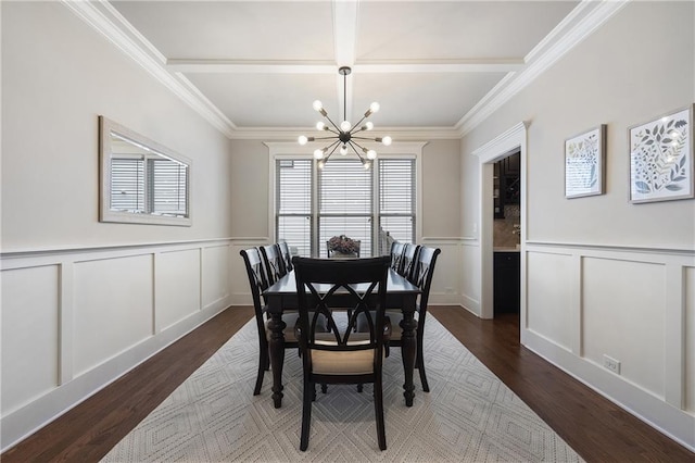 dining area featuring dark wood finished floors, a decorative wall, a chandelier, wainscoting, and crown molding