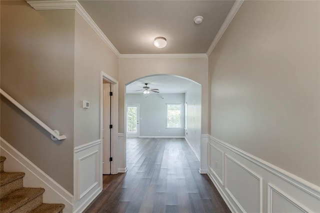 corridor with crown molding, stairway, arched walkways, dark wood-style floors, and a wainscoted wall