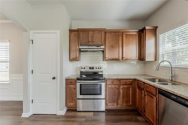 kitchen featuring stainless steel appliances, under cabinet range hood, a sink, dark wood finished floors, and a wainscoted wall
