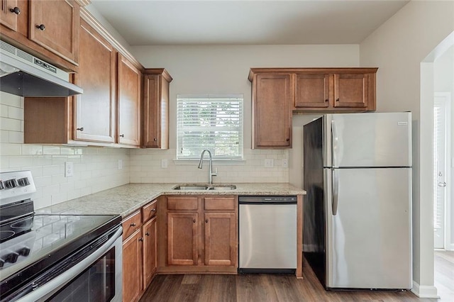 kitchen with stainless steel appliances, a sink, under cabinet range hood, dark wood-style flooring, and light stone counters