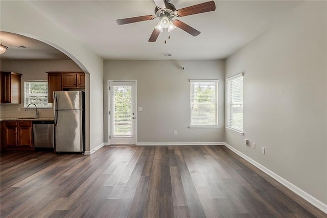 unfurnished dining area with a sink, ceiling fan, dark wood finished floors, baseboards, and arched walkways