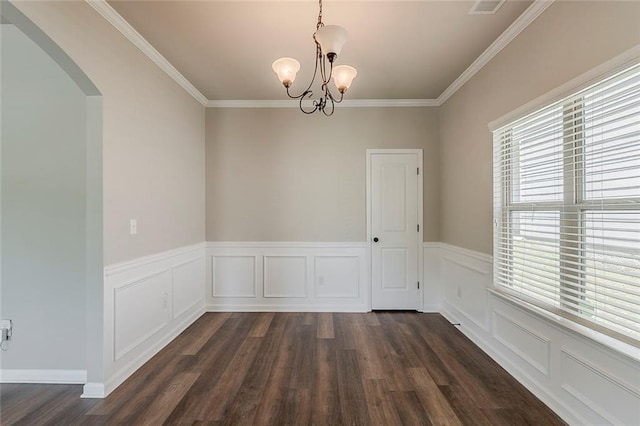 unfurnished dining area with arched walkways, dark wood-style flooring, ornamental molding, a chandelier, and a wainscoted wall