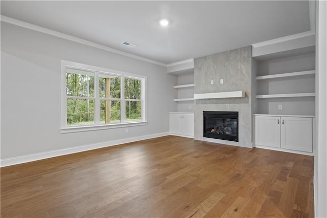 unfurnished living room with a tiled fireplace, wood-type flooring, built in features, and crown molding