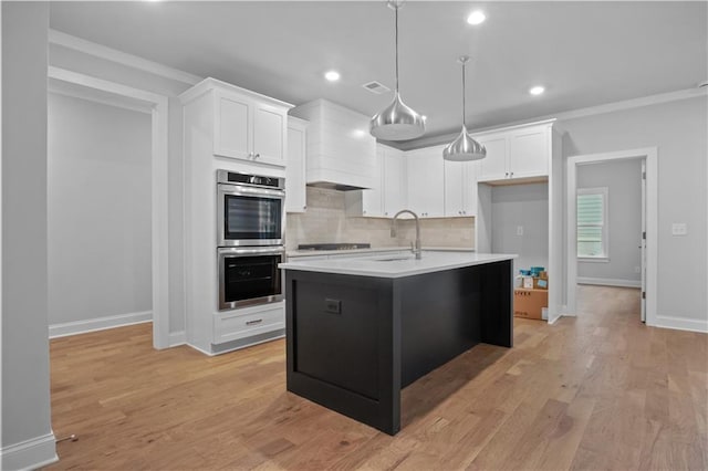 kitchen featuring double oven, white cabinetry, sink, and an island with sink