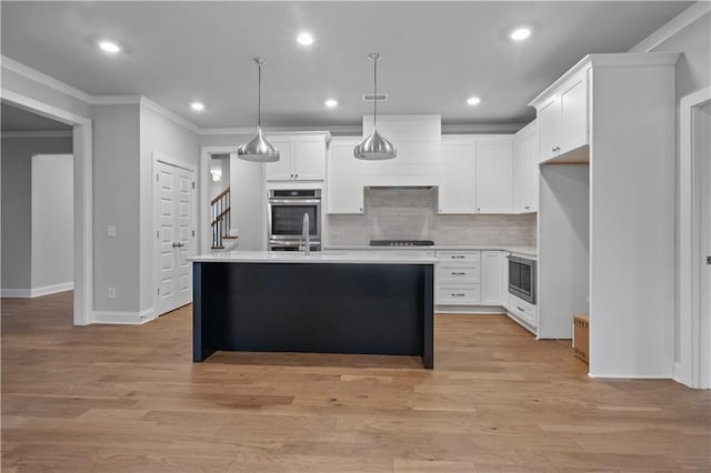 kitchen featuring a kitchen island with sink, white cabinetry, decorative light fixtures, and appliances with stainless steel finishes