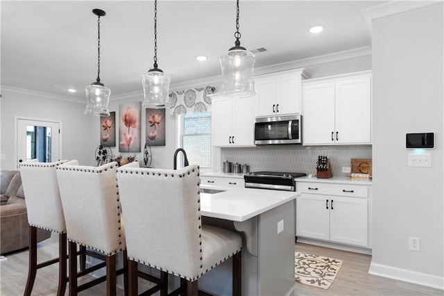 kitchen with stainless steel appliances, decorative light fixtures, a kitchen island with sink, and white cabinets