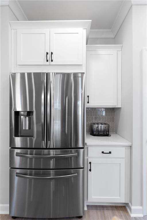 kitchen featuring crown molding, light hardwood / wood-style flooring, stainless steel fridge, white cabinets, and backsplash