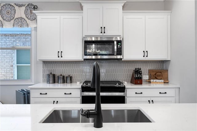 kitchen with tasteful backsplash, black range, and white cabinets